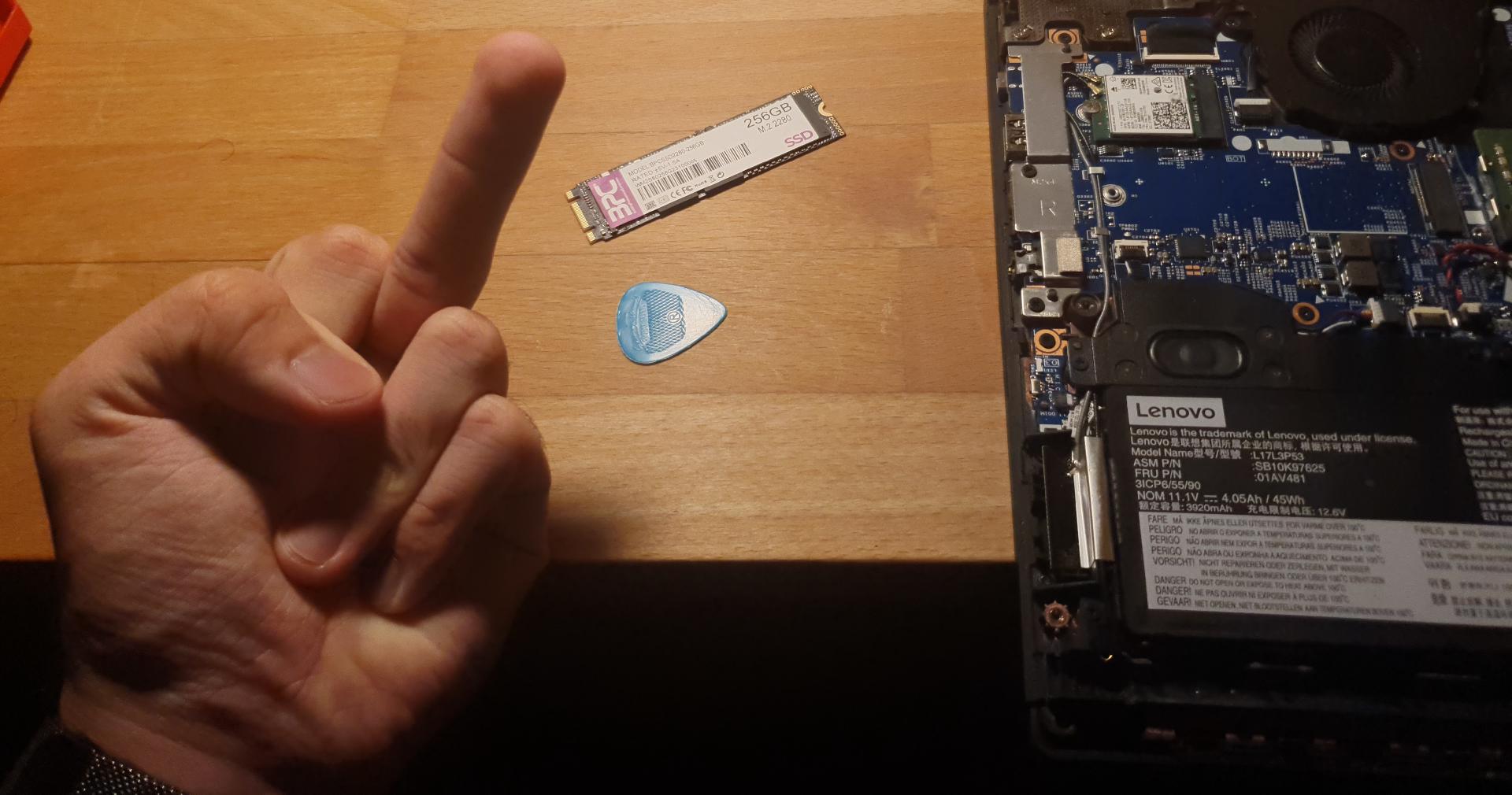 Image of the broken SSD beside the disassembled laptop with a hand flipping the SSD off