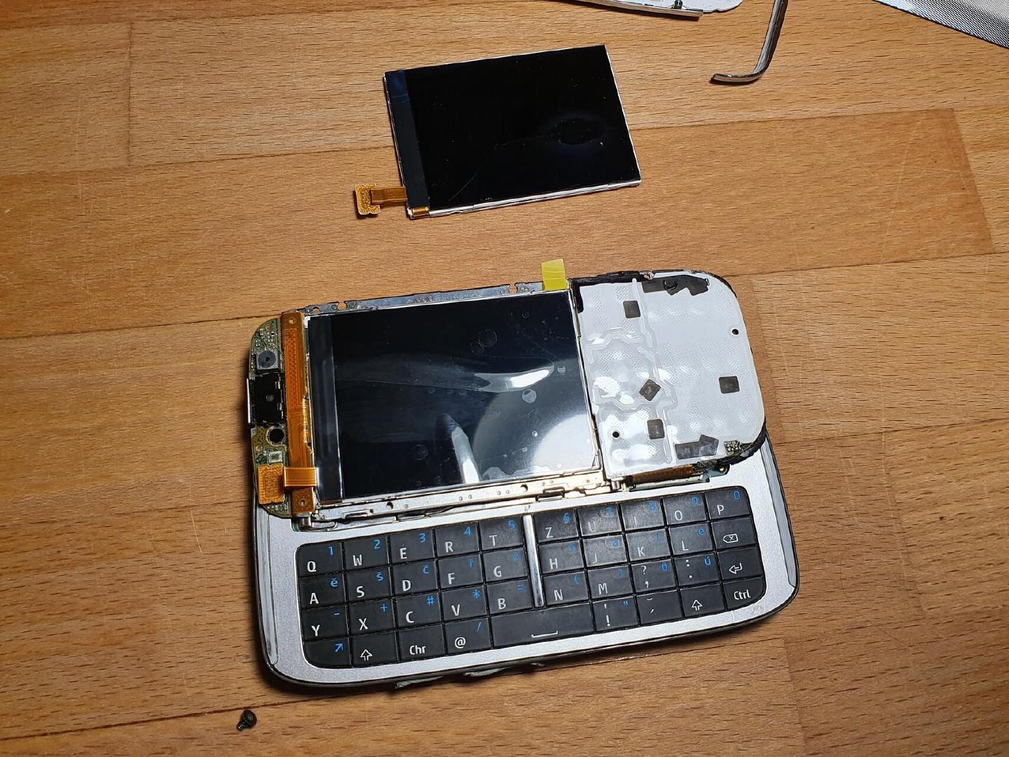 The disassembled phone with the new display inserted and the old and broken one in the background.